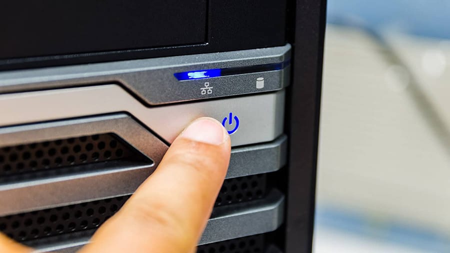 A finger is pressing the power button on a desktop computer.