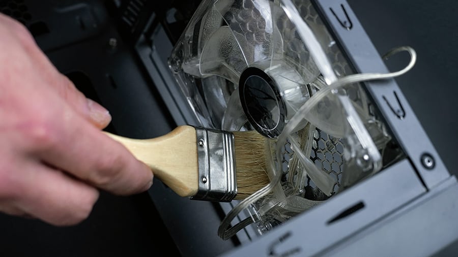 Cleaning a dirty computer case fan with a brush.