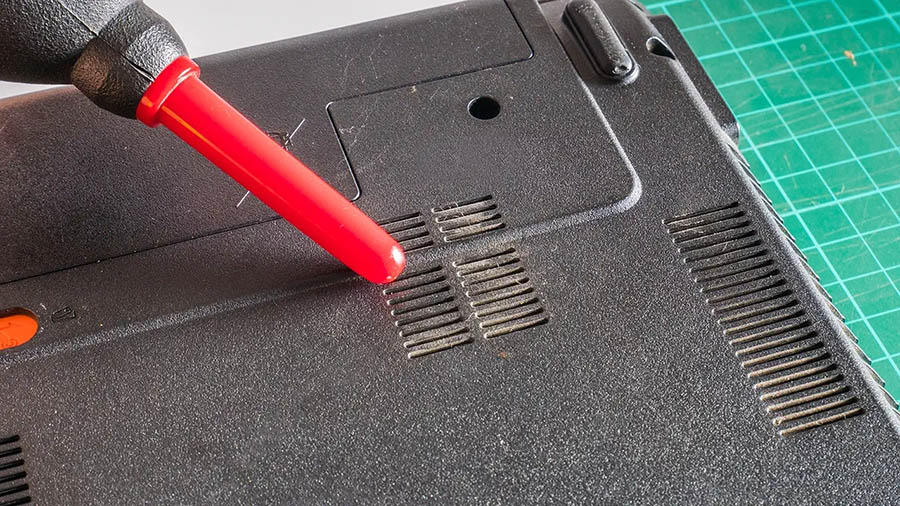 A manual pump blower is being used to remove the dust from a Chromebook's vents.