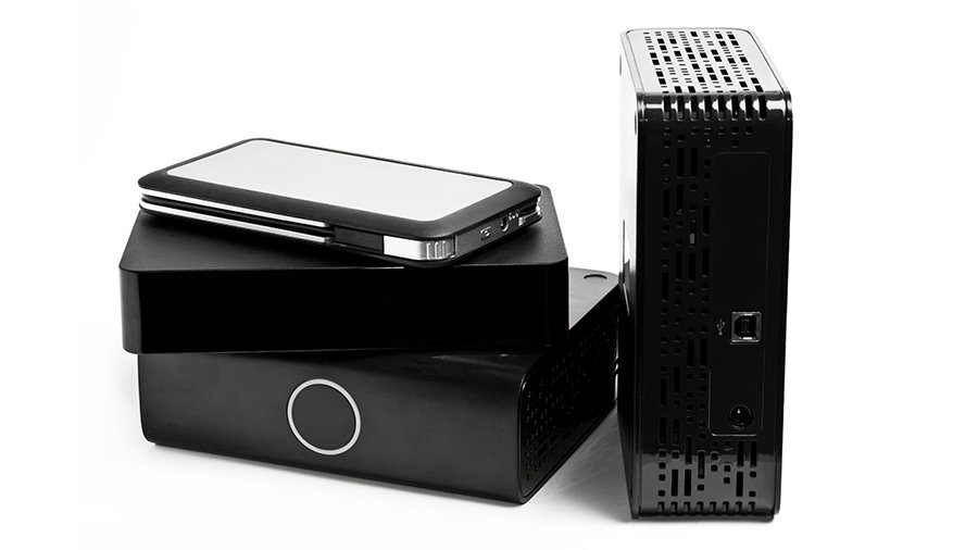 Different types of external hard drives enclosed stacked on top of each other and one beside the pile.