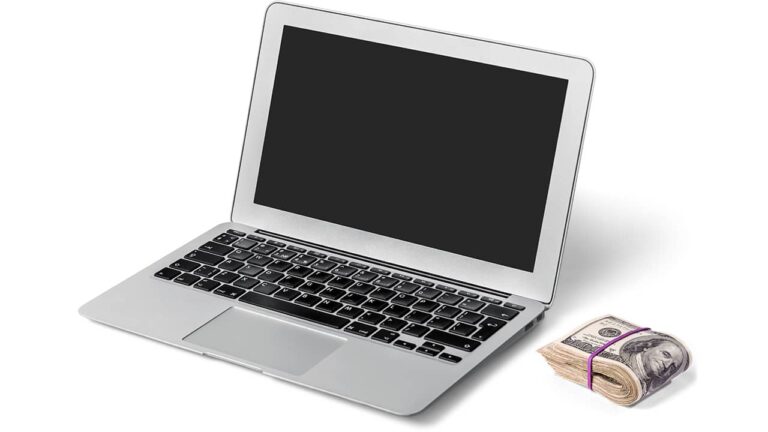 An Apple MacBook laptop with cash placed beside it.