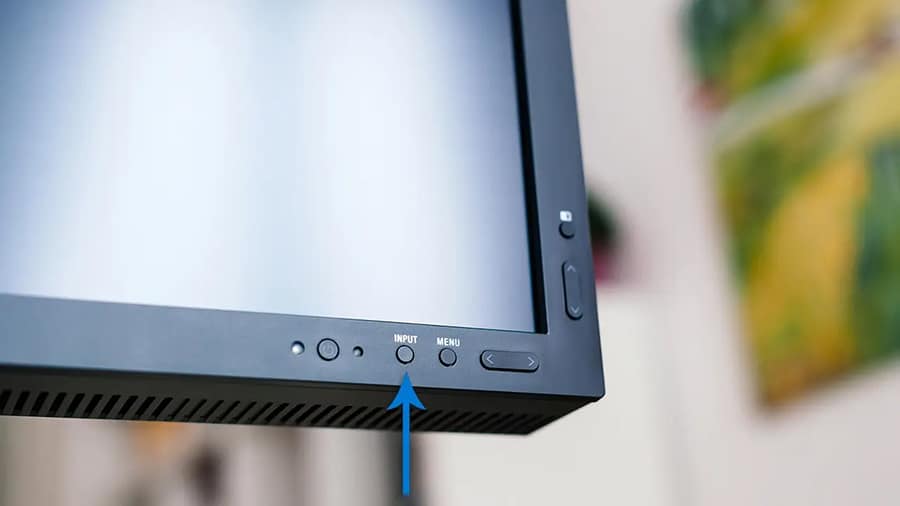 An arrow is pointing to a monitor's input source select button.