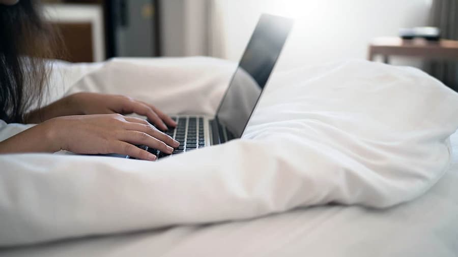 A woman is using a laptop on a bed which is inhibiting airflow.