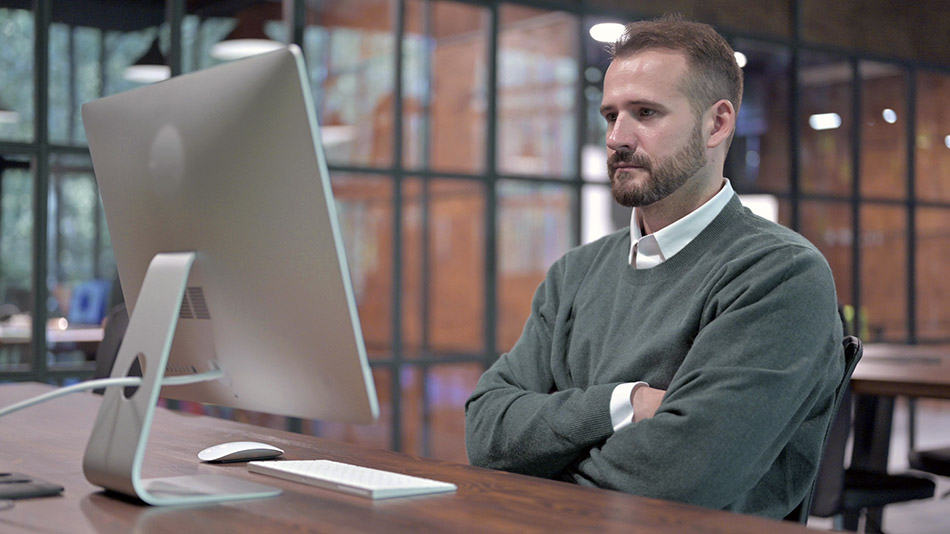 A man is reading an article on a computer monitor.